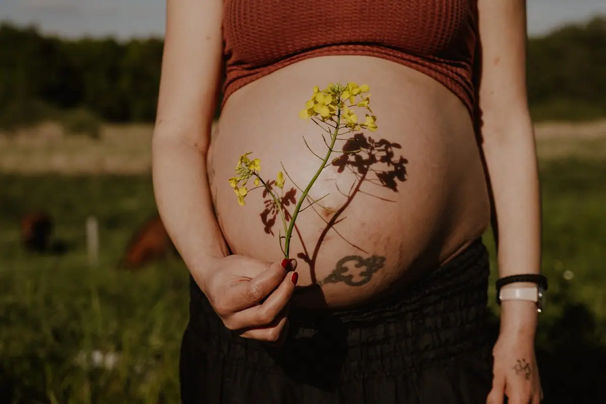 Detailaufnahme mit Rapsblüte vom Babybauch beim Babybauchshooting in Bensheim