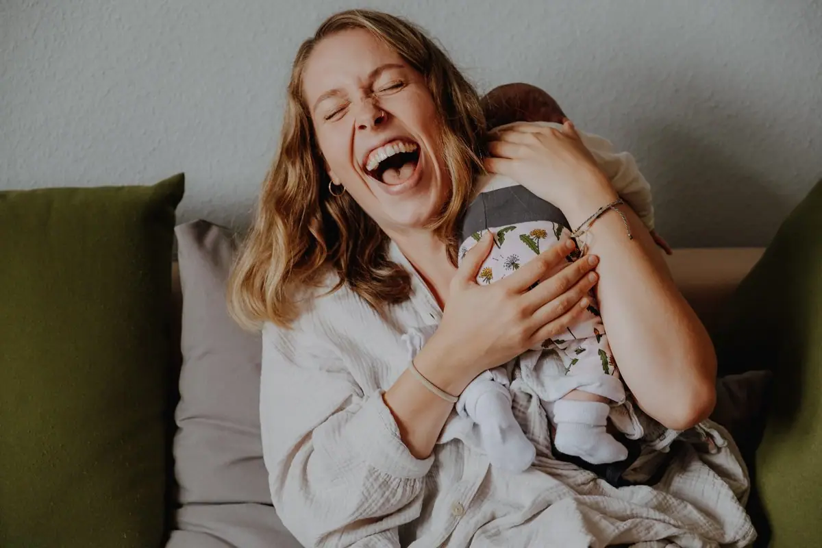 Wochenbettreportage, Lachende Mama mit Neugeborenem auf dem Arm beim Stillen