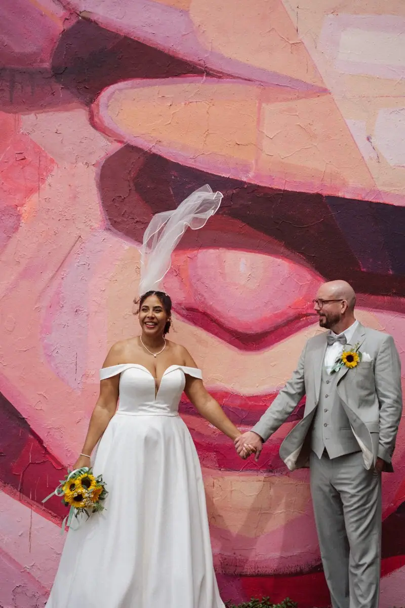Brautpaar vor einem rosa Wandbild