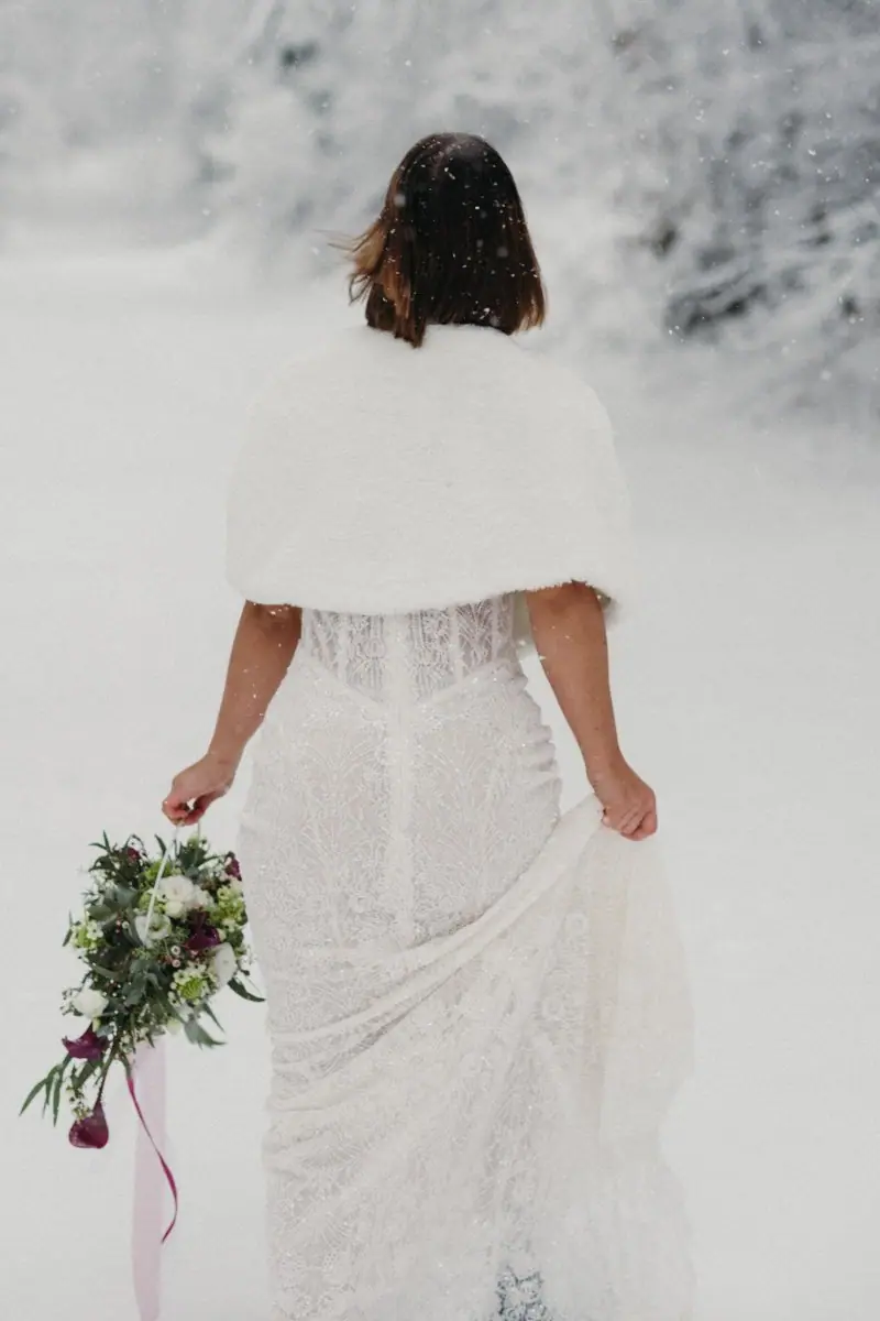 Braut mit Stola und Strauß im Schnee, von hinten