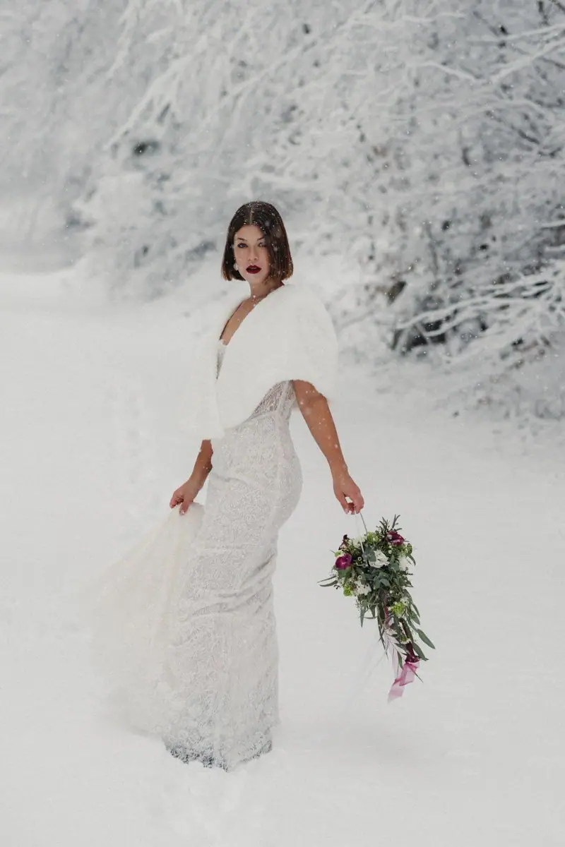 Braut im Spitzenkleid zwischen verschneiten Bäumen